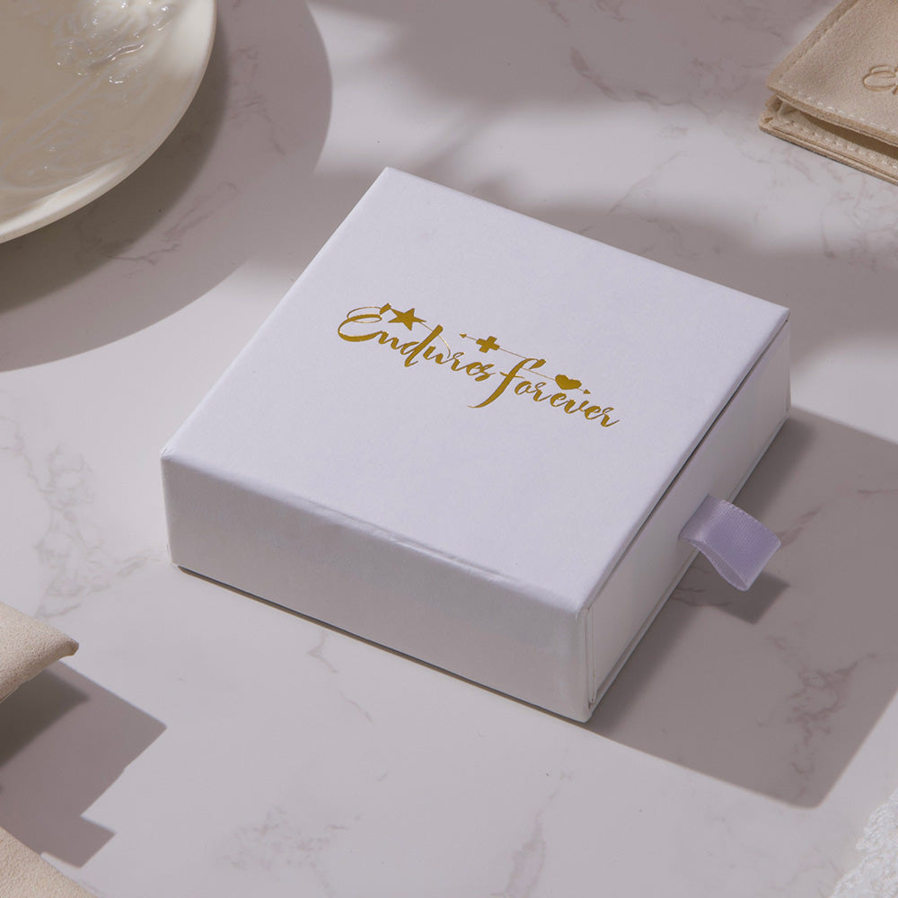White jewelry box with 'Endures forever' text on a marble surface