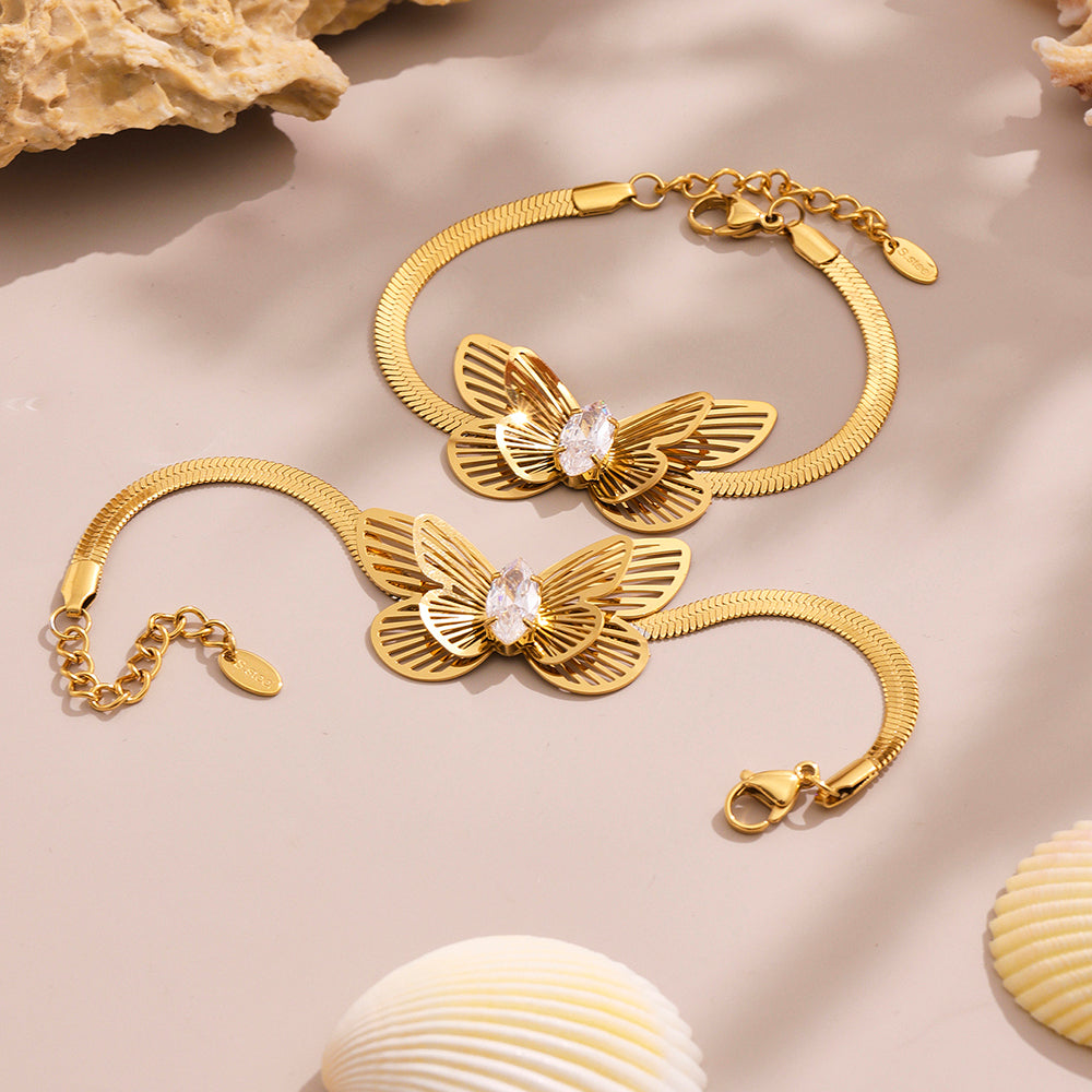 Gold butterfly-themed bracelet on a beige surface with shells