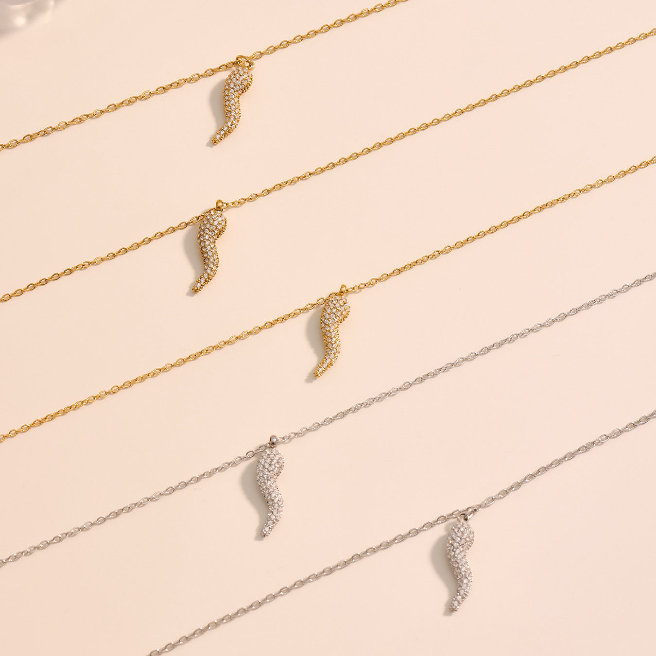 Three gold and silver necklaces with leaf-shaped pendants on a beige background
