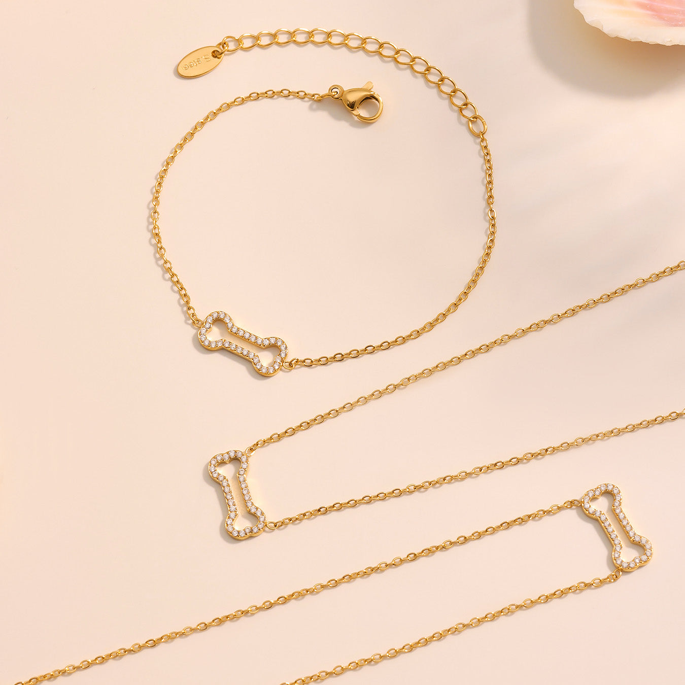 Gold bracelet and necklace with bone-shaped pendants on a light pink background