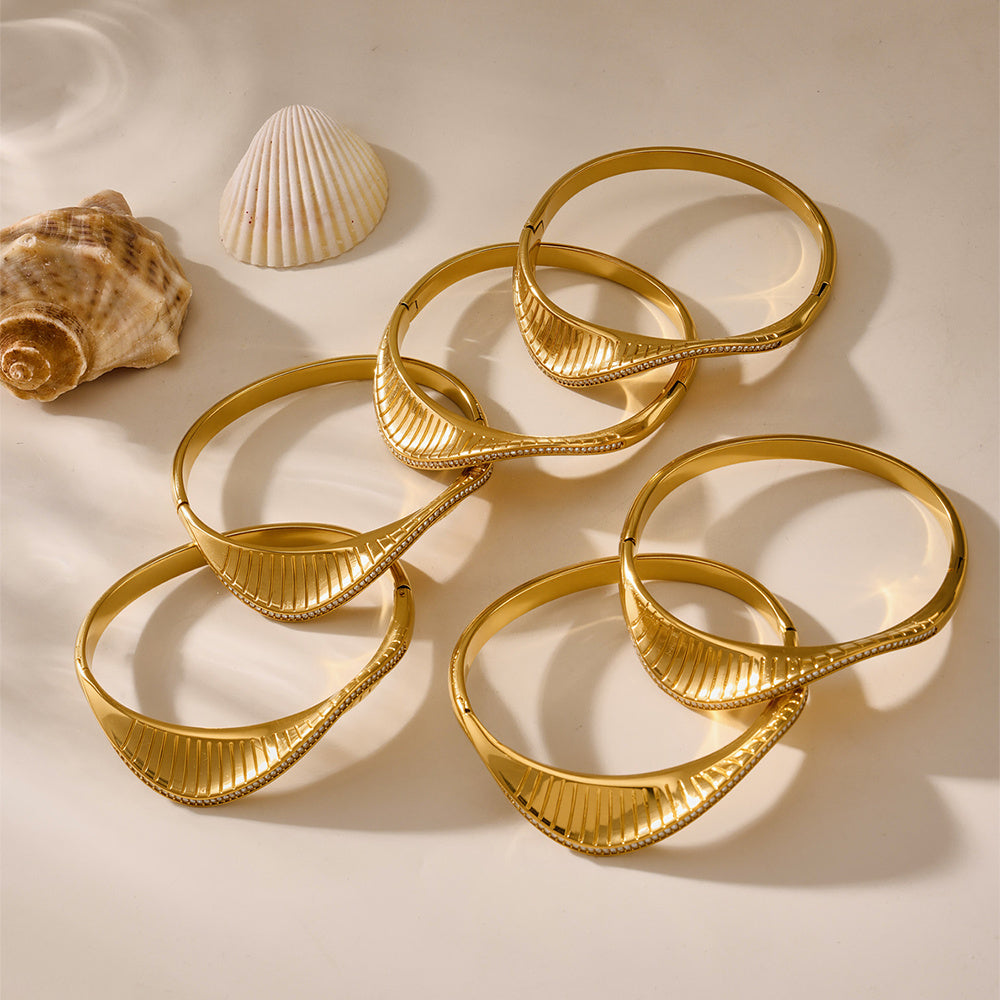 Set of gold bangles on a beige surface with two shells.
