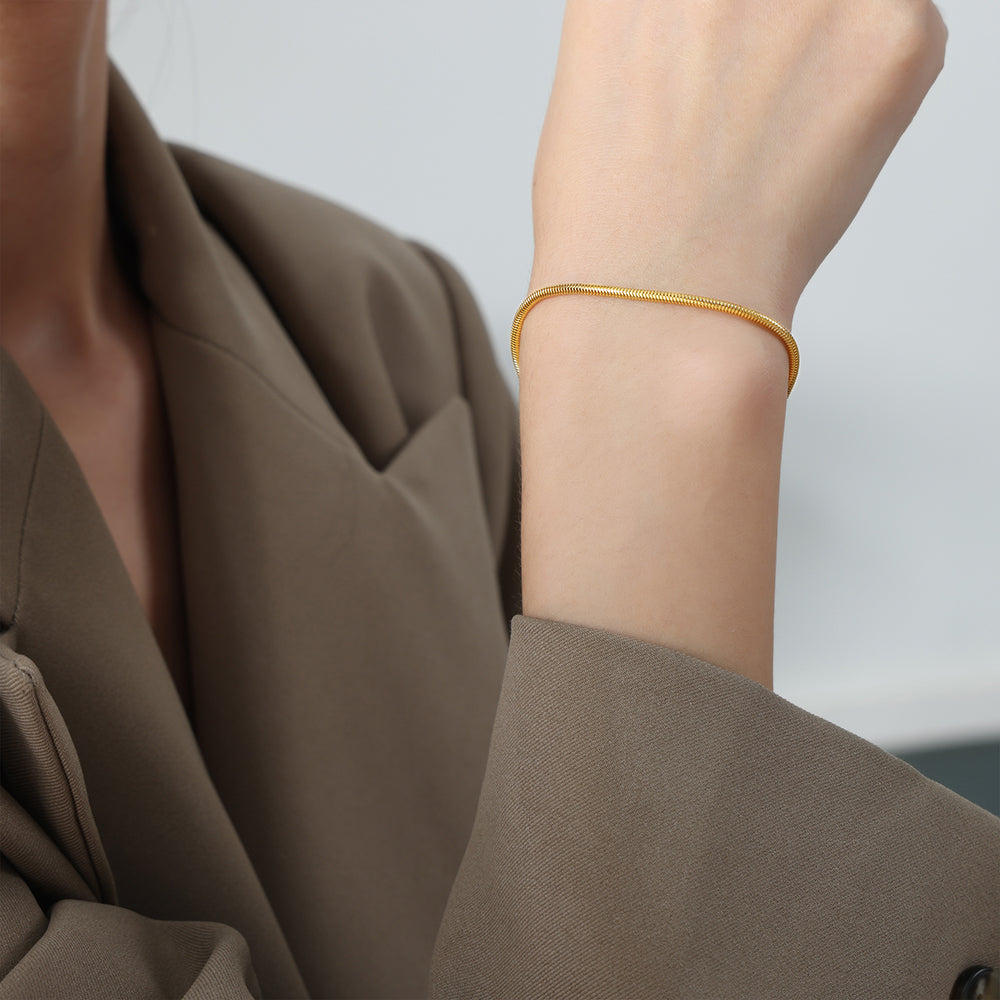 Person wearing a gold bracelet on a plain background