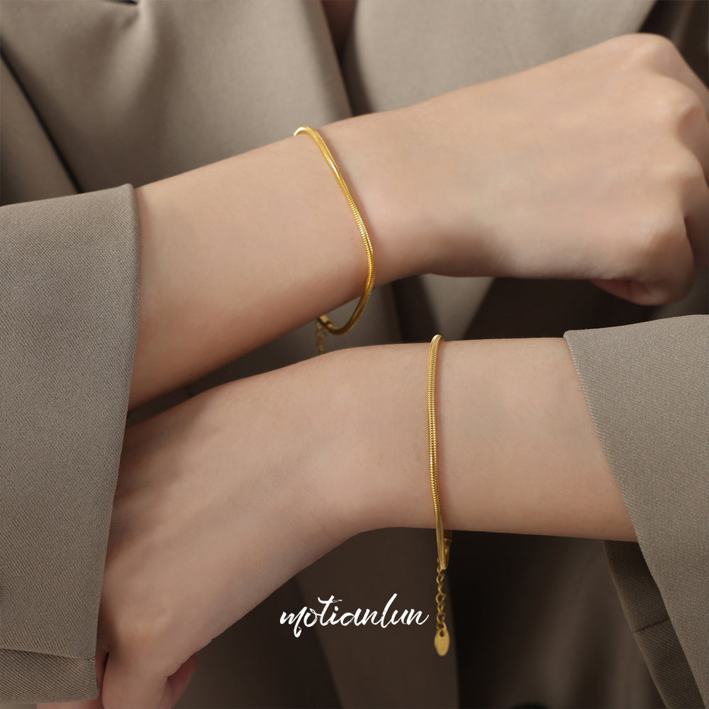 Two gold bracelets on a person's wrist with a neutral background