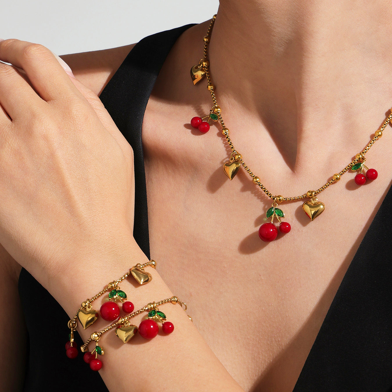 Gold necklace and bracelet with cherry charms on a person wearing a black top.