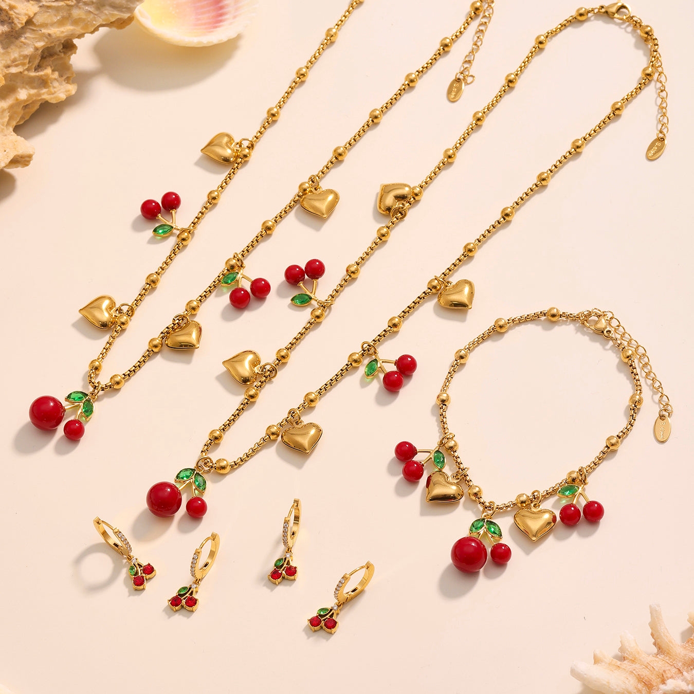 Gold jewelry set with cherry and heart charms on a beige background
