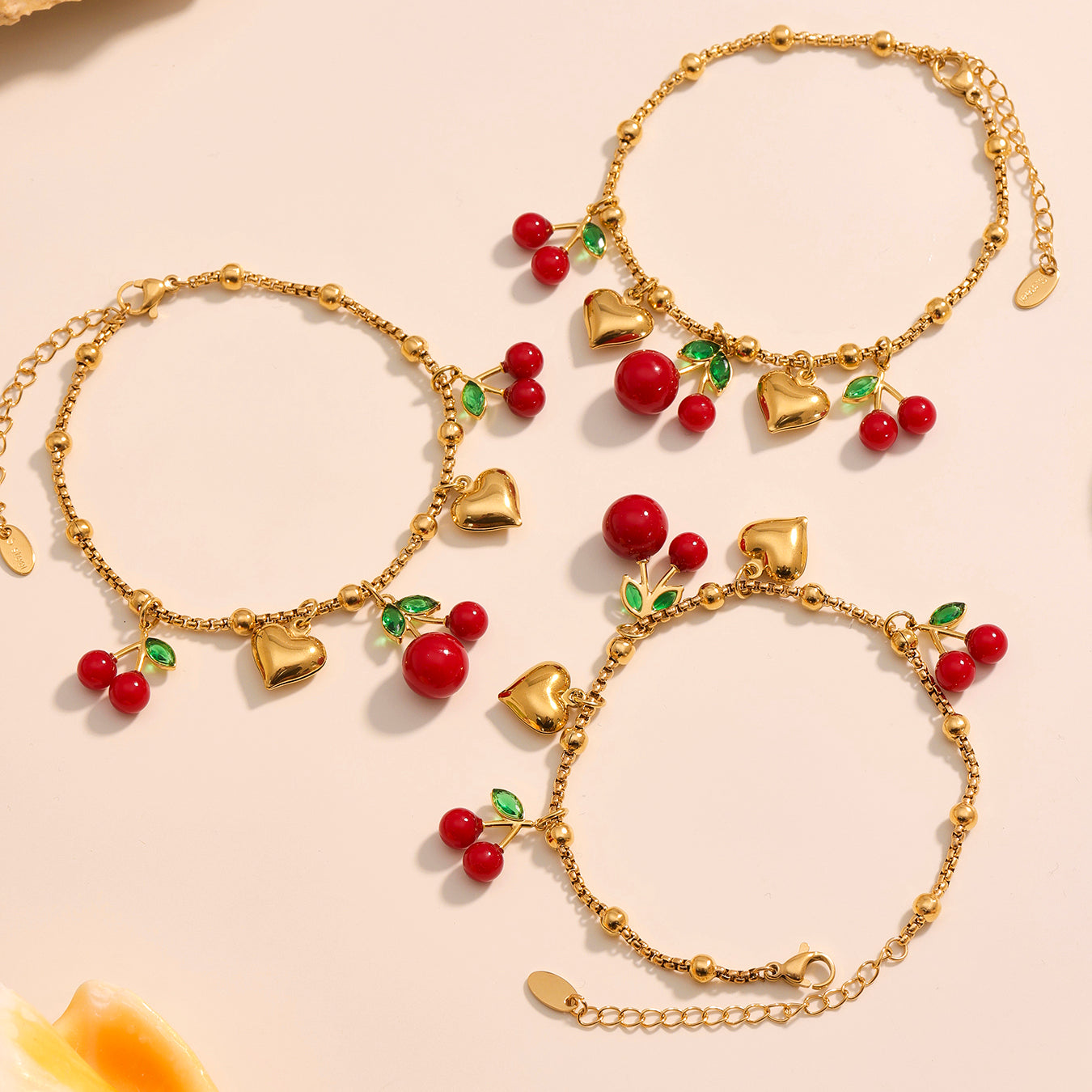 Gold bracelets with heart and cherry charms on a beige background