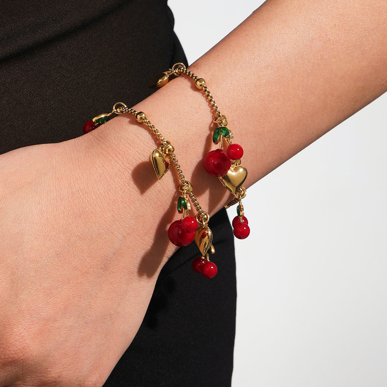 Gold bracelet with red berry charms on a wrist against a neutral background