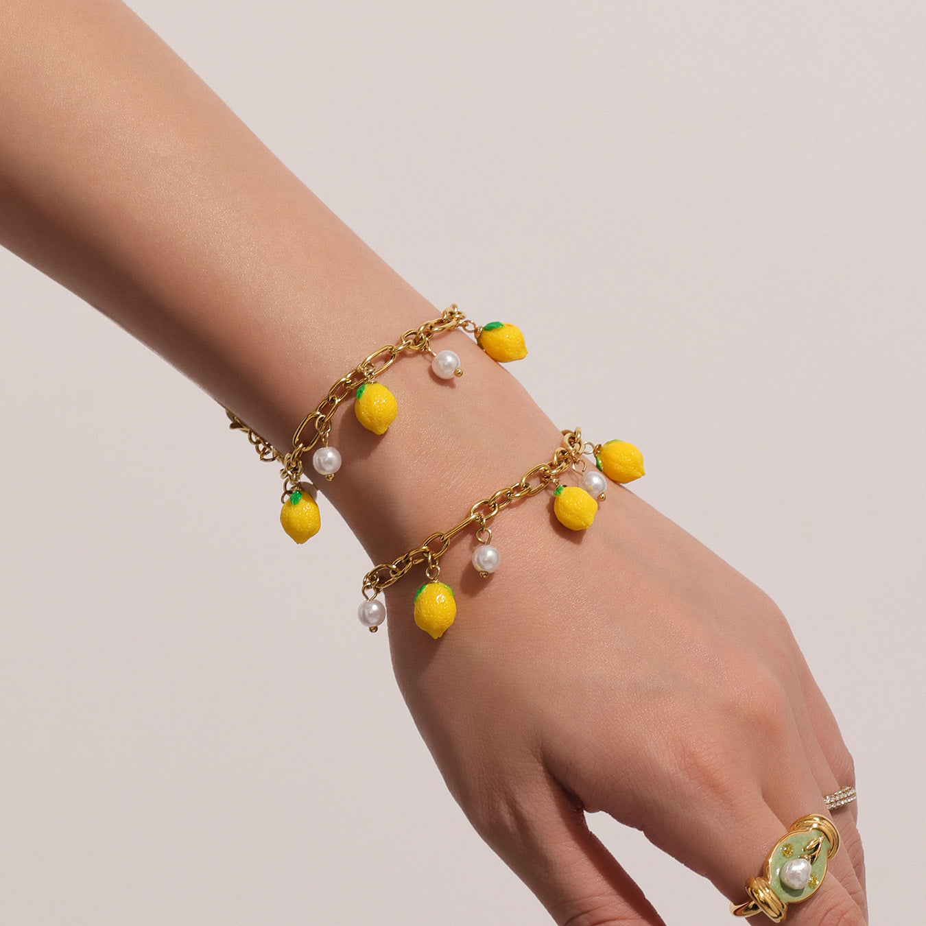 Gold bracelet with lemon and pearl charms on a hand against a plain background