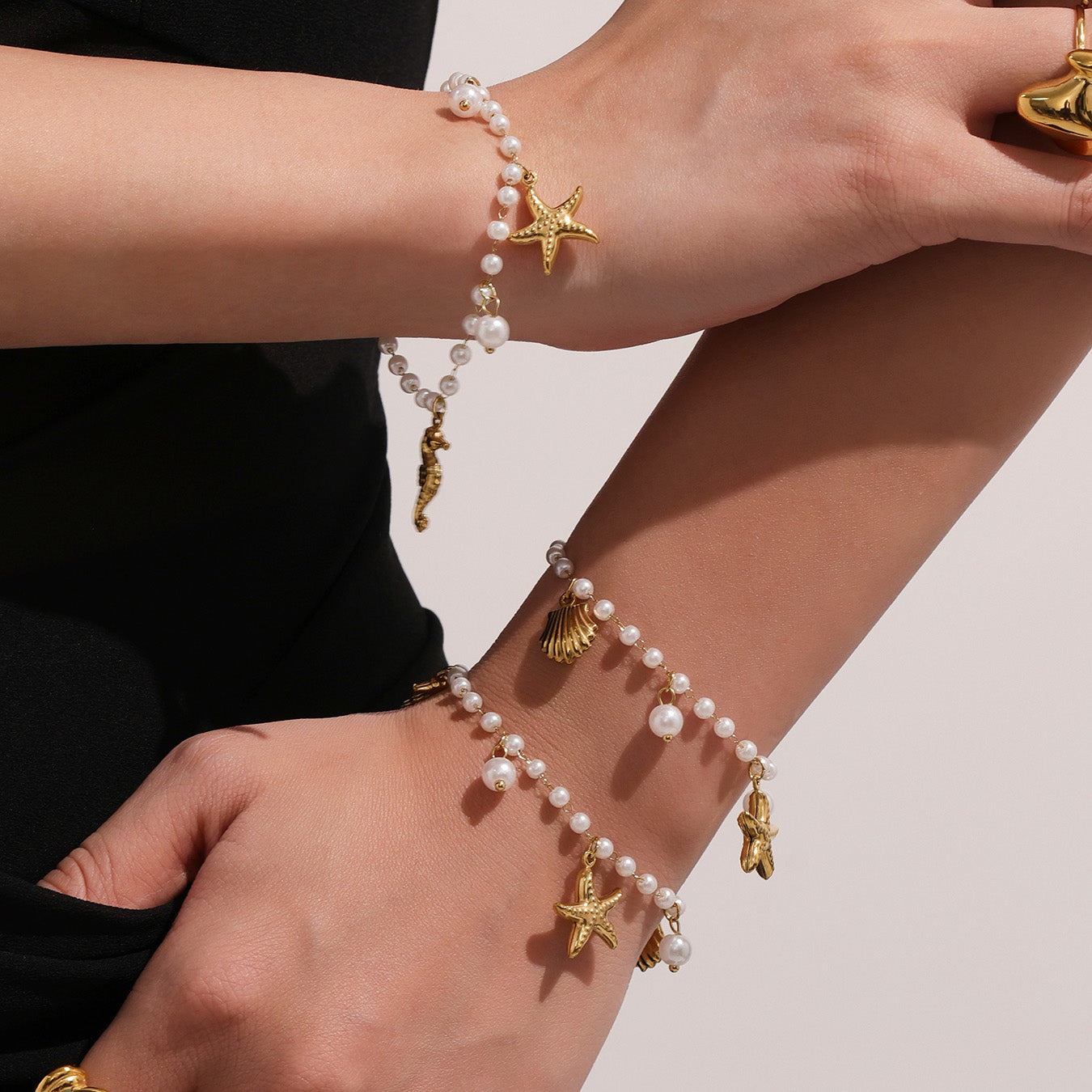 Close-up of a person's wrist wearing multiple pearl and gold charm bracelets on a light background