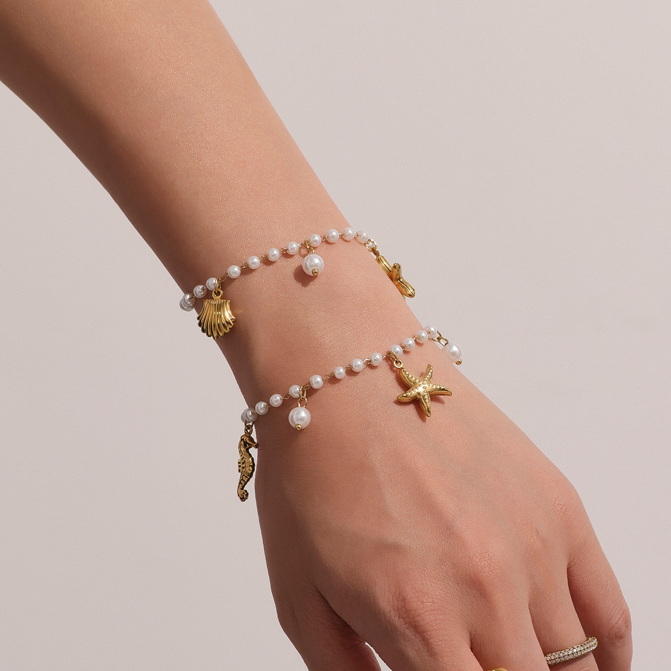 Hand wearing a pearl bracelet with gold starfish and shell charms on a plain background