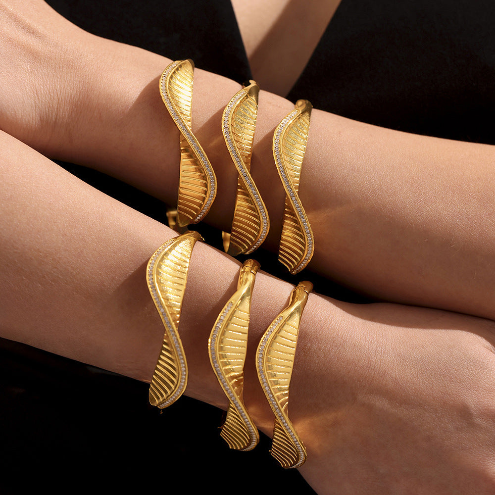 Gold leaf-shaped bracelets on a person's wrist against a black background