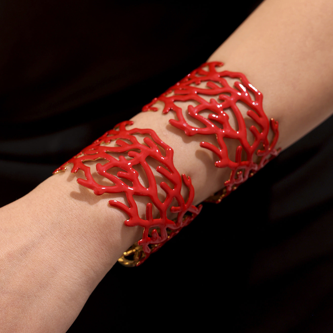 Coral red open bangle with coral texture worn on wrist, set against a dark background