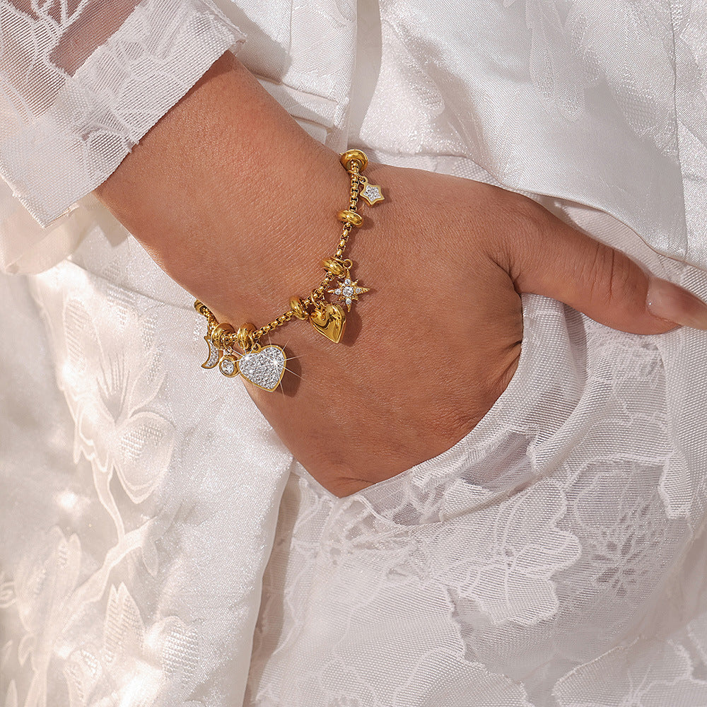 Gold charm tennis bracelet with heart stud CZ details worn on wrist with lace background