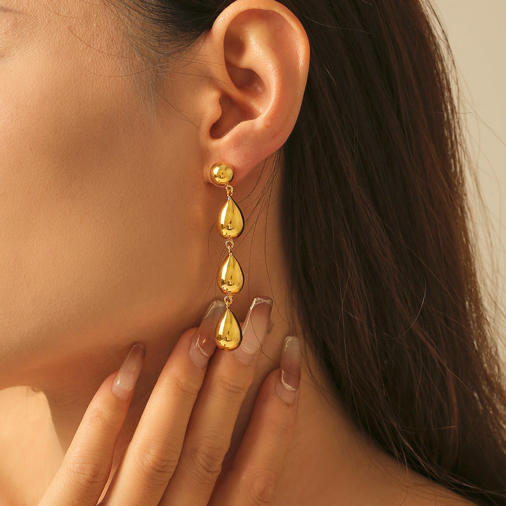 Close-up of a woman wearing gold teardrop earrings with a neutral background