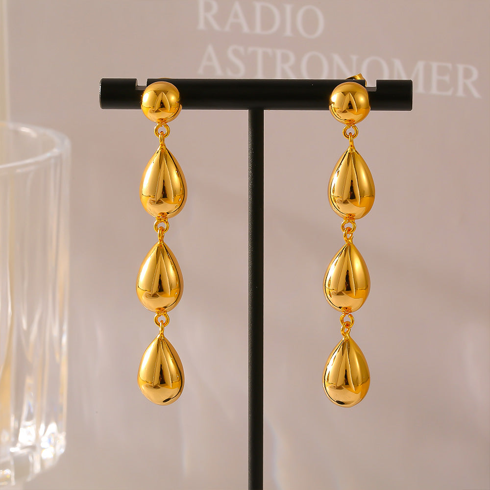 Gold teardrop earrings on a display stand with a blurred background