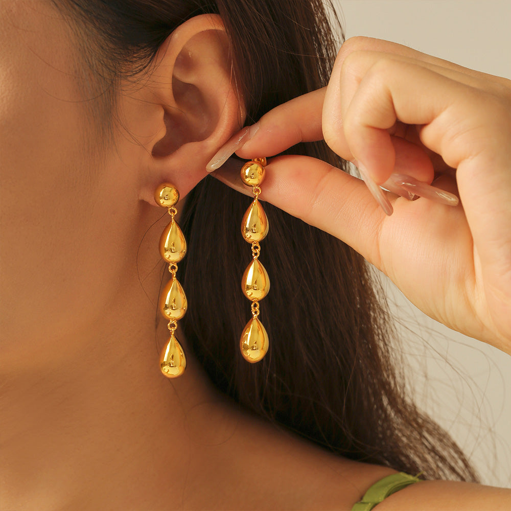 Gold teardrop earrings being worn by a person with a neutral background