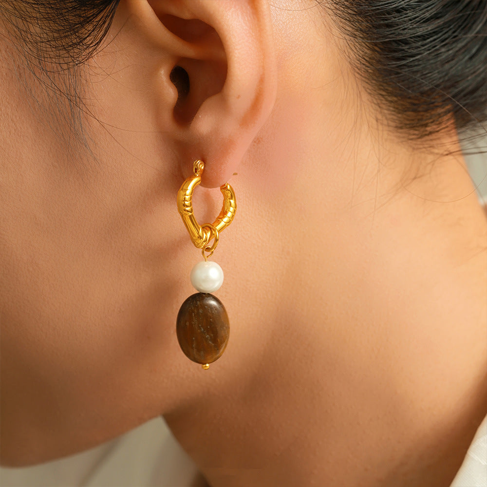 Gold hoop earring with a brown and white bead worn by a person.