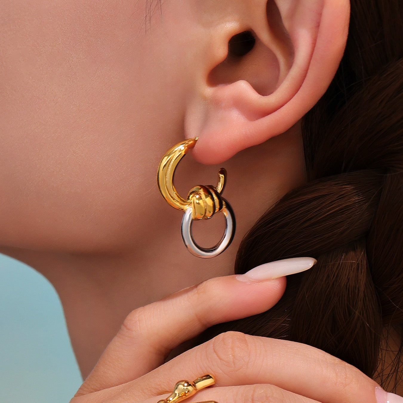 Close-up of a person wearing a gold and silver hoop earring.