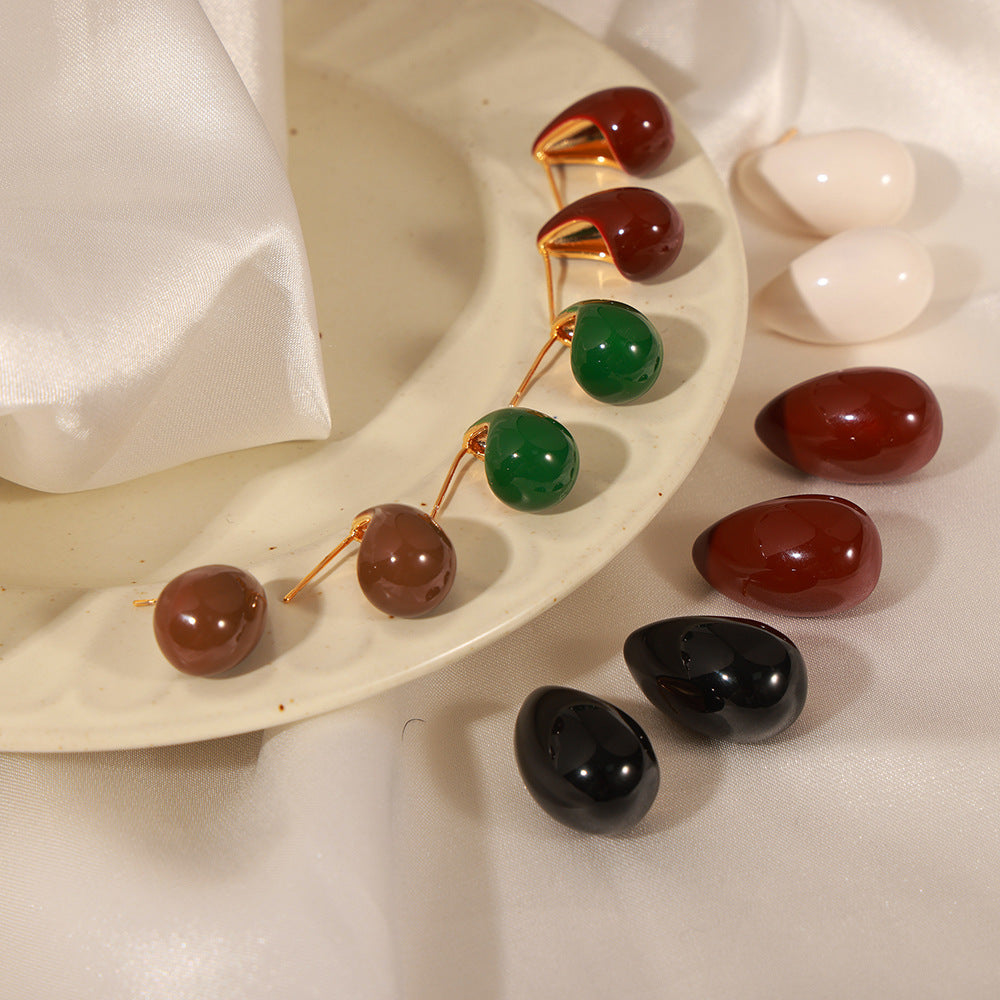 Decorative earrings with red, green, and black stones on a white plate.