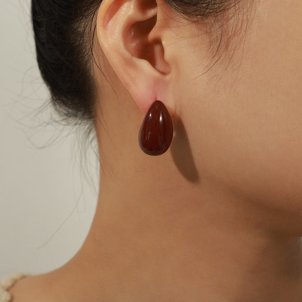 Close-up of a person wearing a teardrop-shaped earring on a neutral background