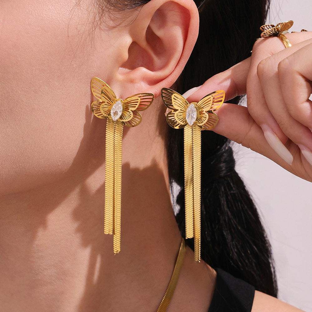 Gold butterfly earrings with tassels worn by a person