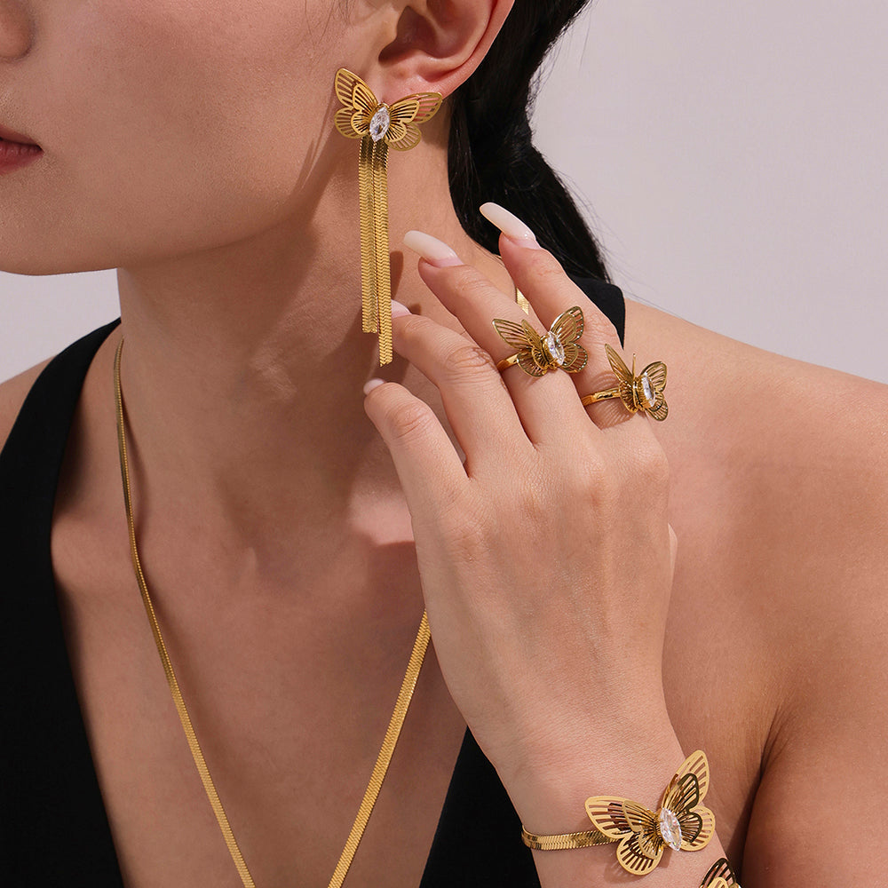 Gold butterfly earrings, ring, and bracelet on a model against a neutral background