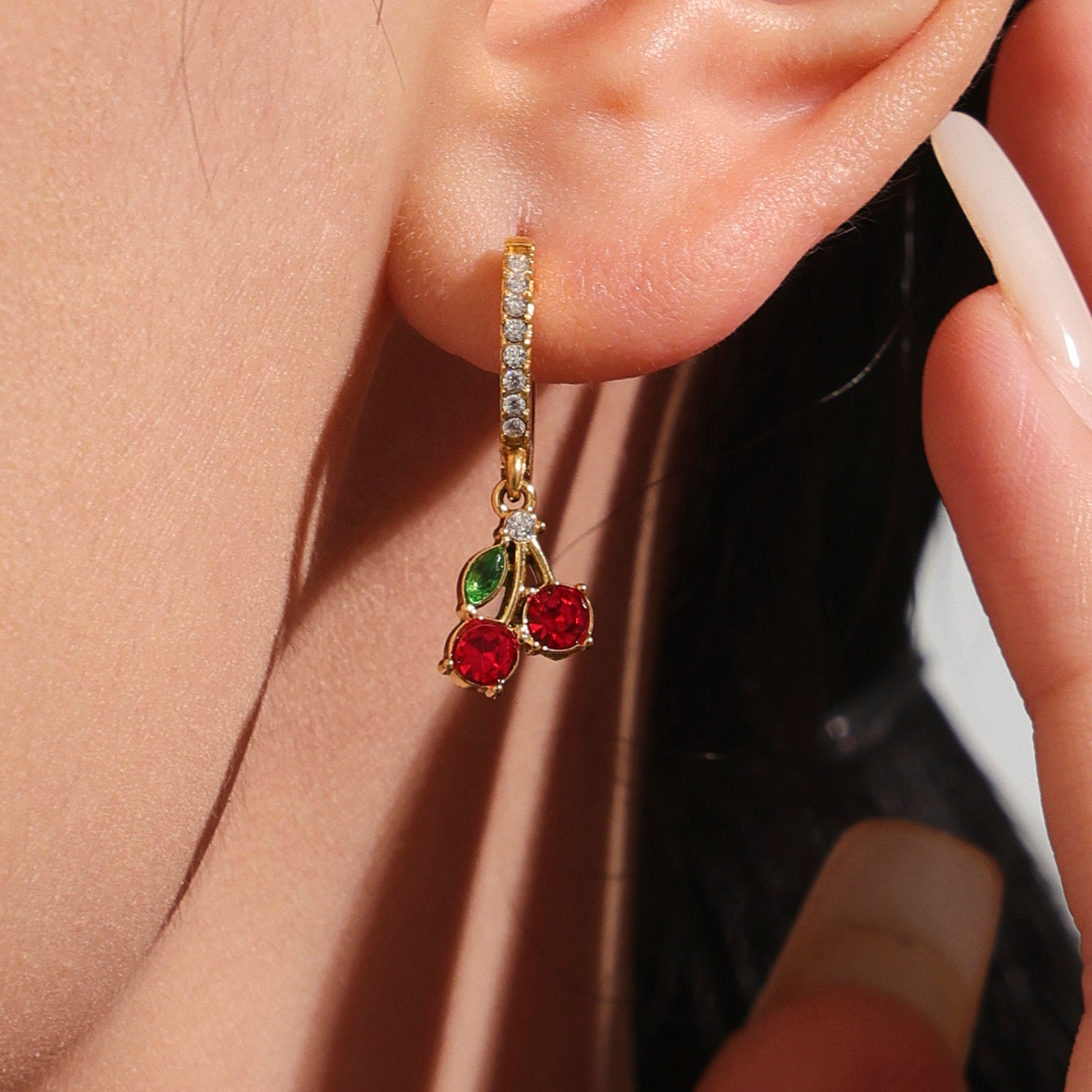 Close-up of a gold earring with red and green gemstones worn on an ear.