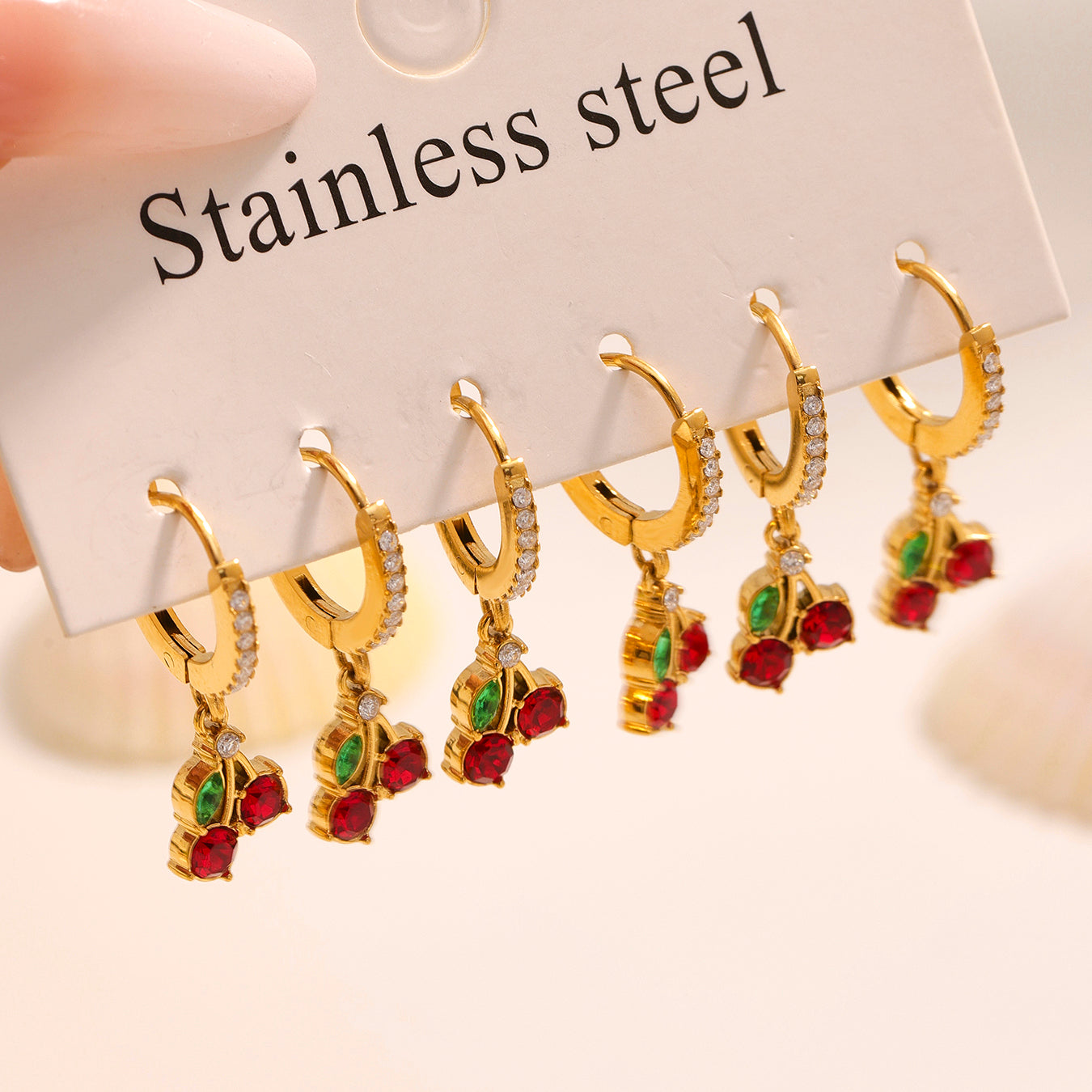 Gold earrings with red and green gemstones on a 'Stainless steel' card.