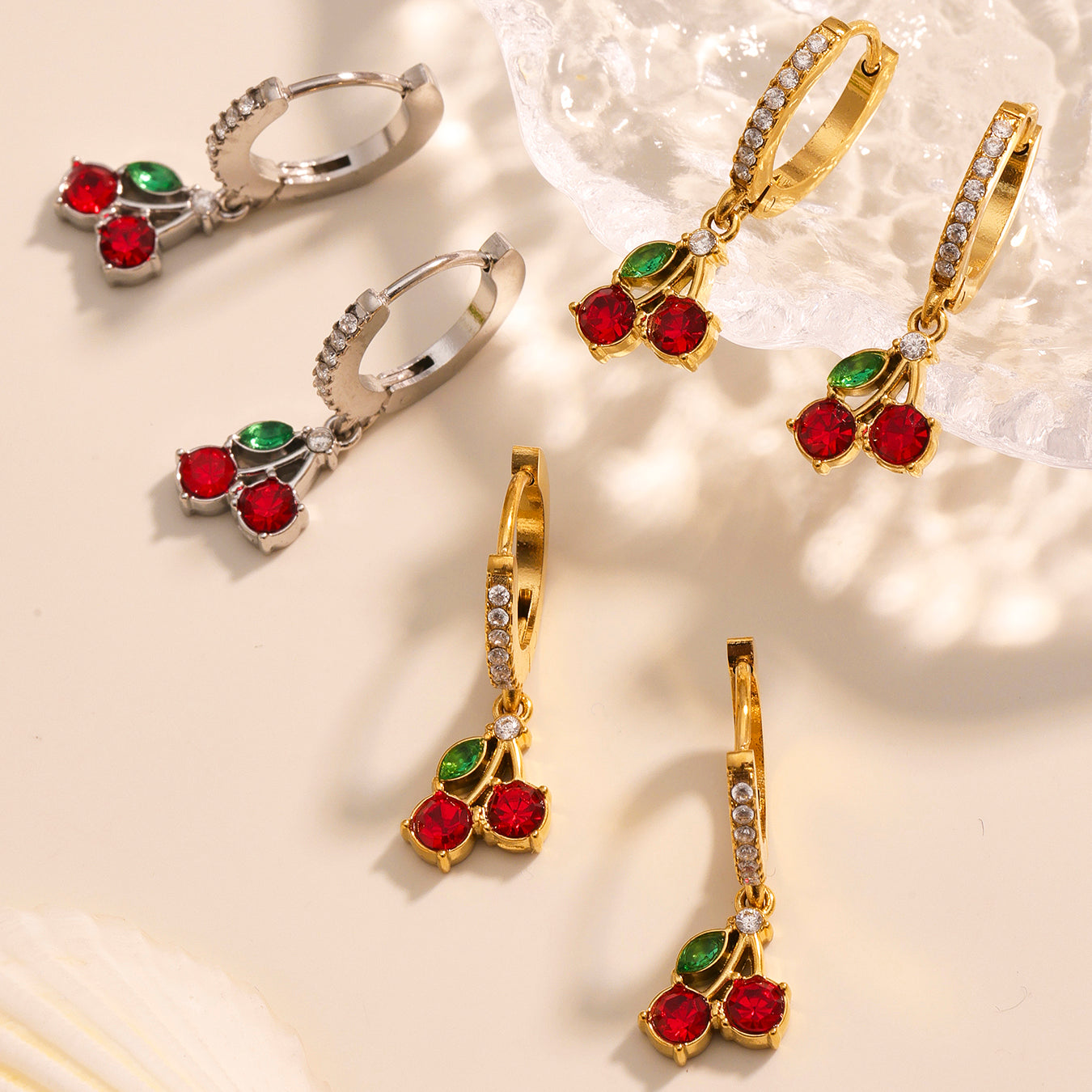 Pair of gold and silver earrings with red and green gemstones on a light background