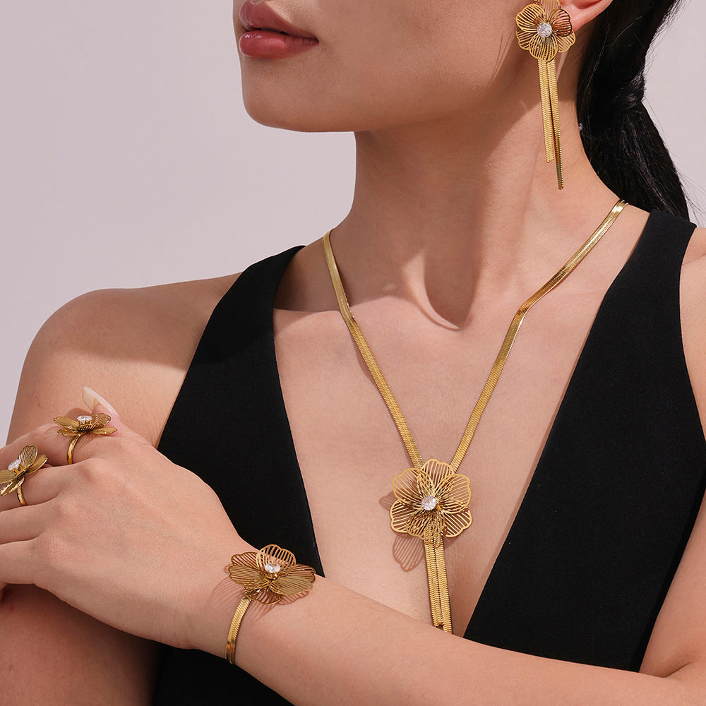 Woman wearing gold jewelry including a necklace, earrings, and bracelet on a plain background