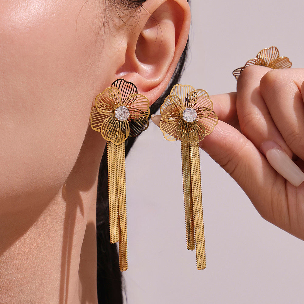 Gold floral earrings with tassels worn by a person against a neutral background