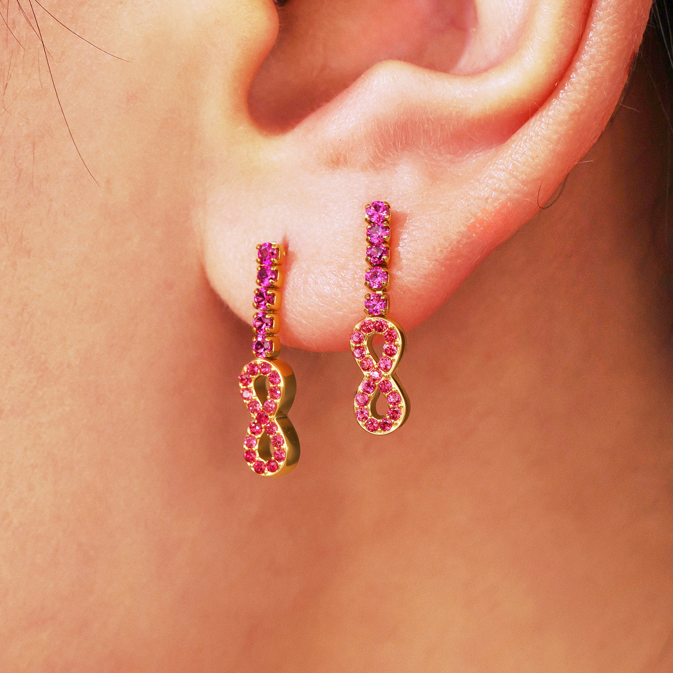 Gold earrings with pink gemstones worn on an ear
