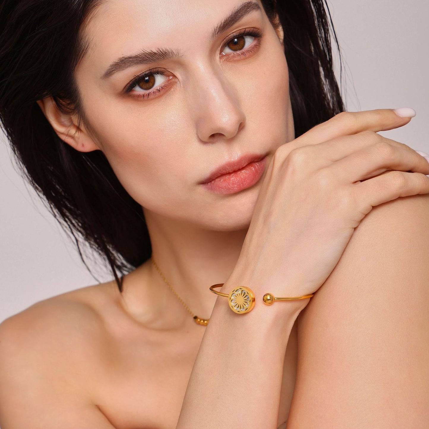 Close-up of woman wearing gold bracelets and necklace on neutral backdrop