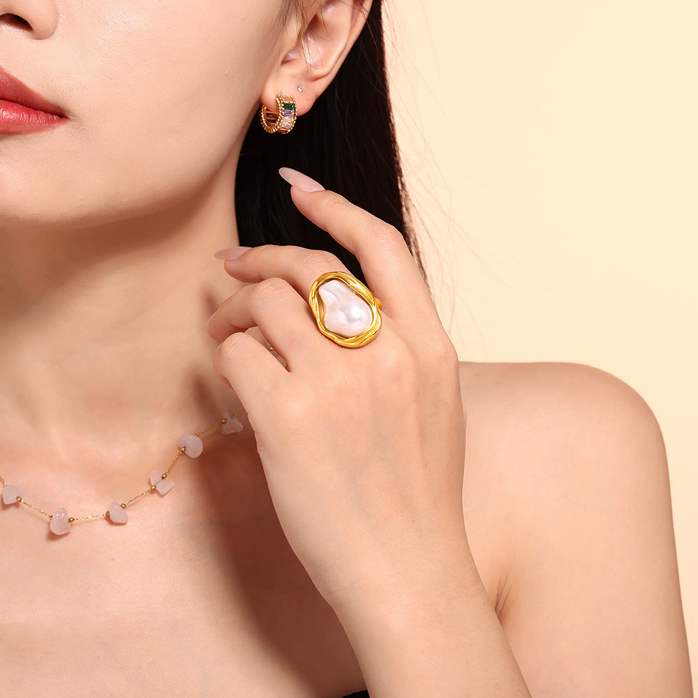 Close-up of a woman wearing gold rings and pearl jewelry styled on a beige backdrop