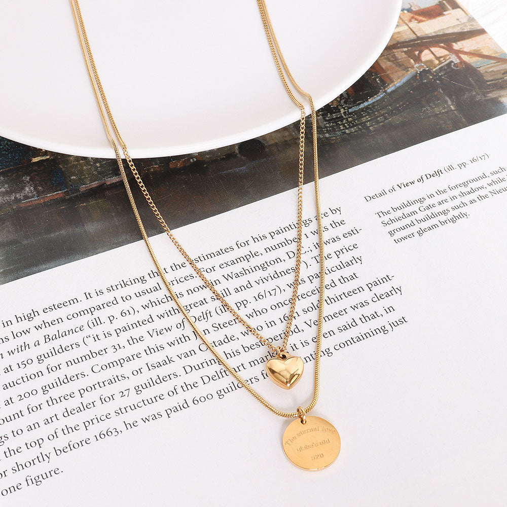 Flatlay of romantic peach heart charm necklace with gold stainless steel layers placed on newspaper – perfect for soft aesthetic content