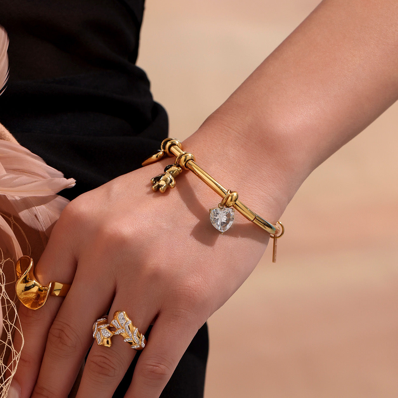 Model wearing gold charm bracelet and ring on wrist with soft background