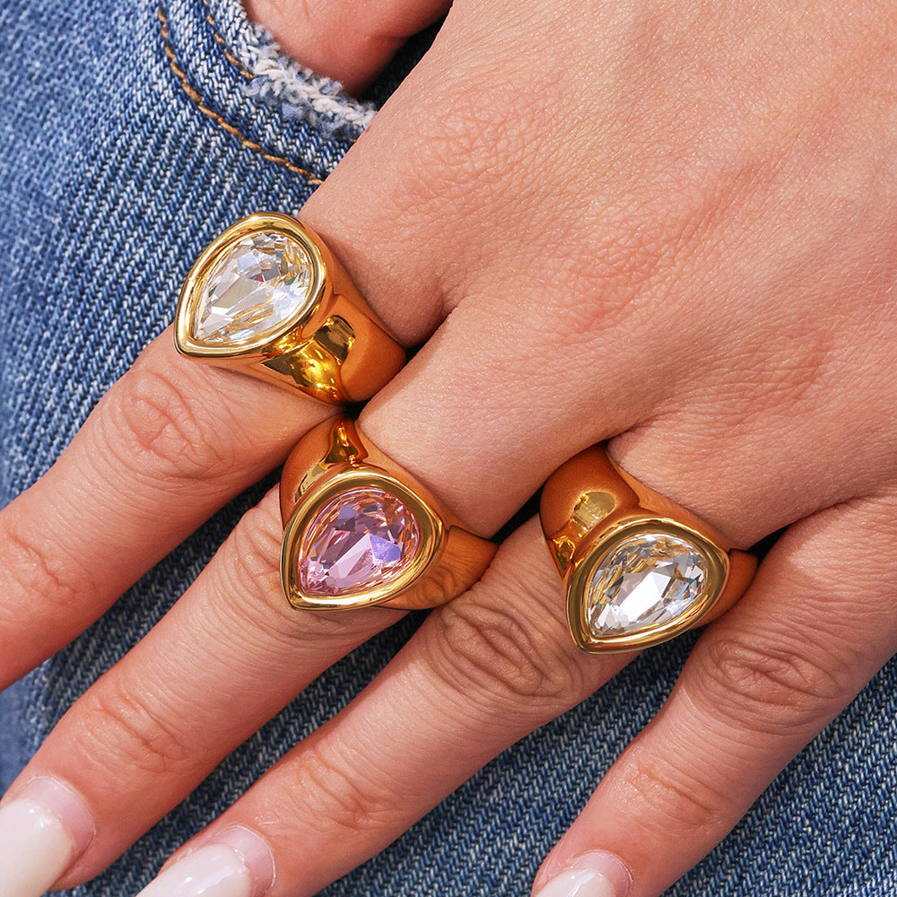Gold chunky zircon rings with teardrop gemstones worn on a hand, against a denim background.
