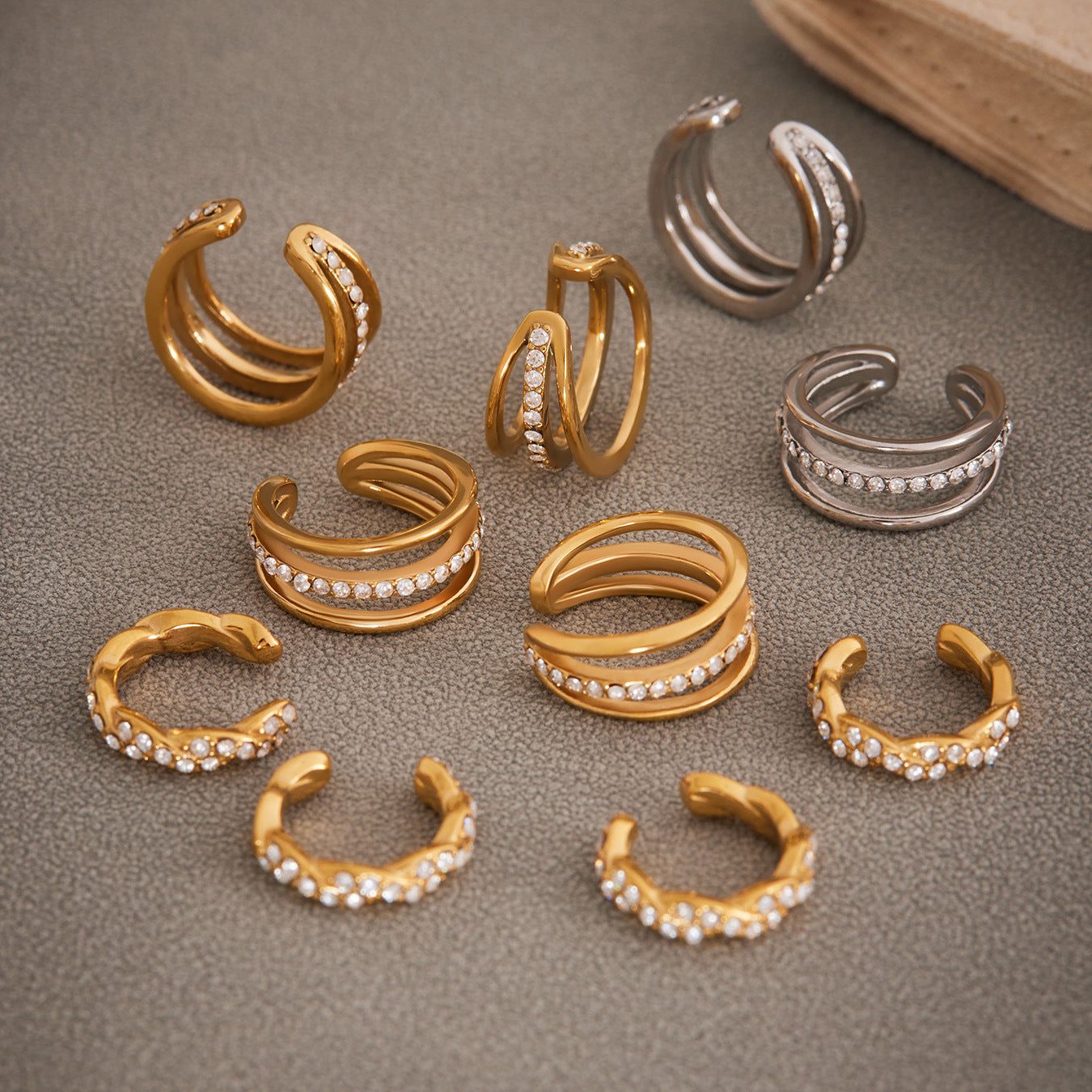 Collection of multiple gold ear cuffs with zircon stones, elegant minimalist jewelry display.