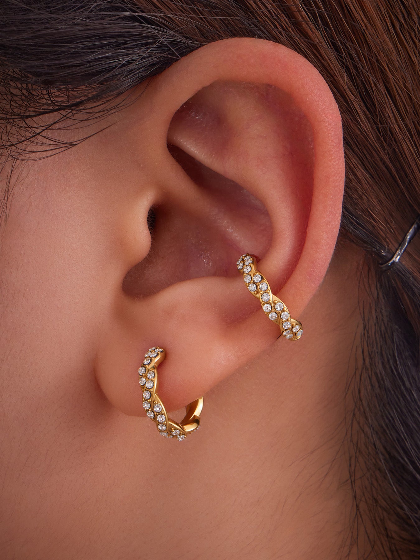 Layered ear stacking style with gold ear cuff and other gold hoop earrings.
