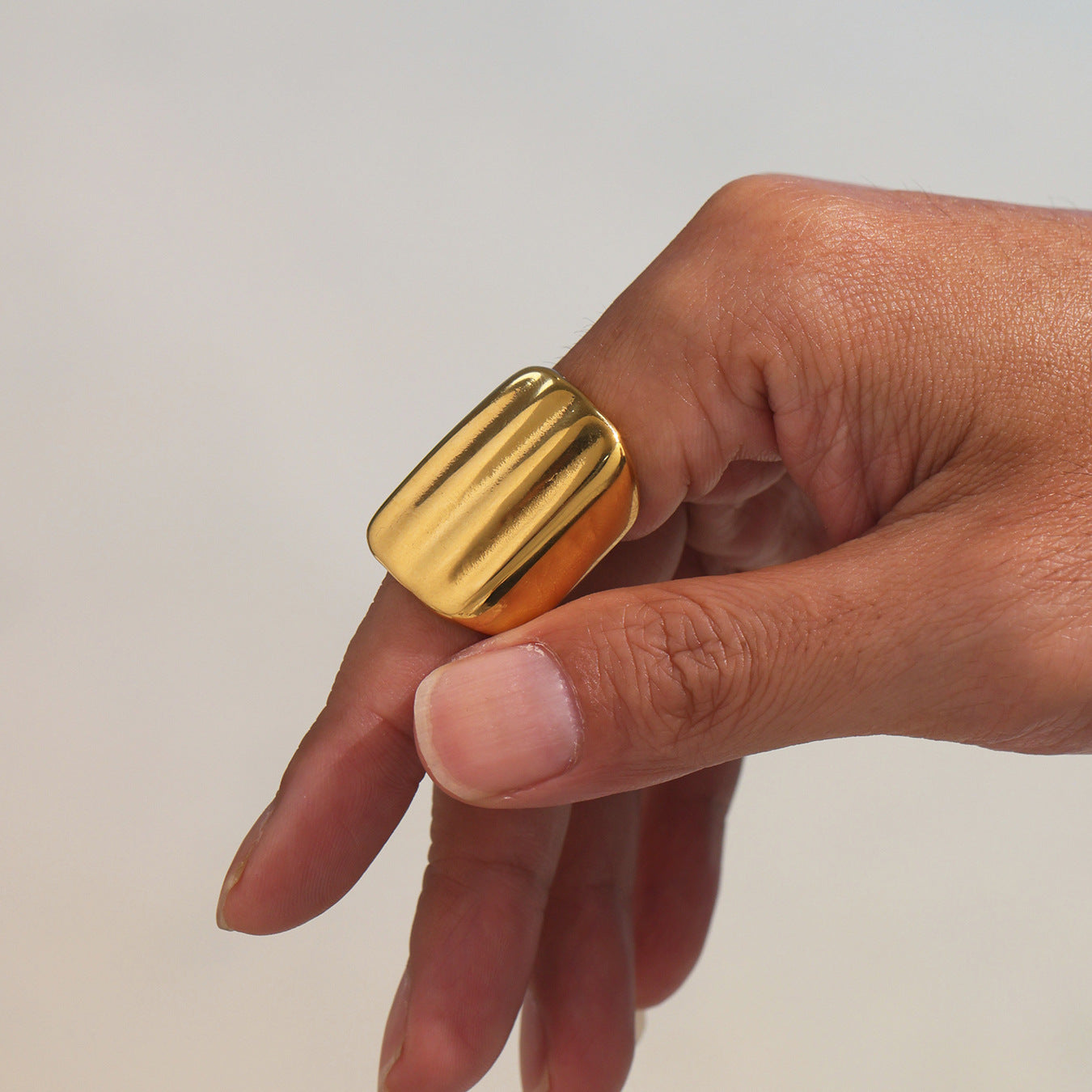 Gold stainless steel ring worn on a finger against a neutral background.