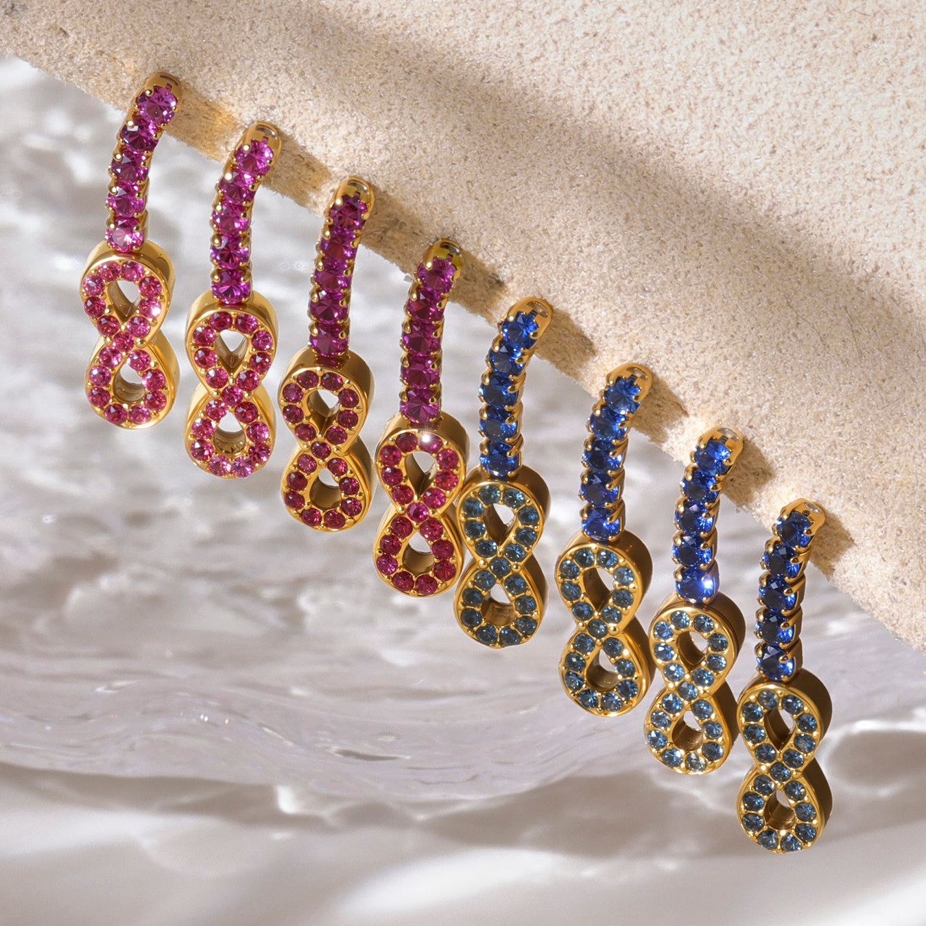 Pair of gold earrings with pink and blue gemstones on a textured beige surface
