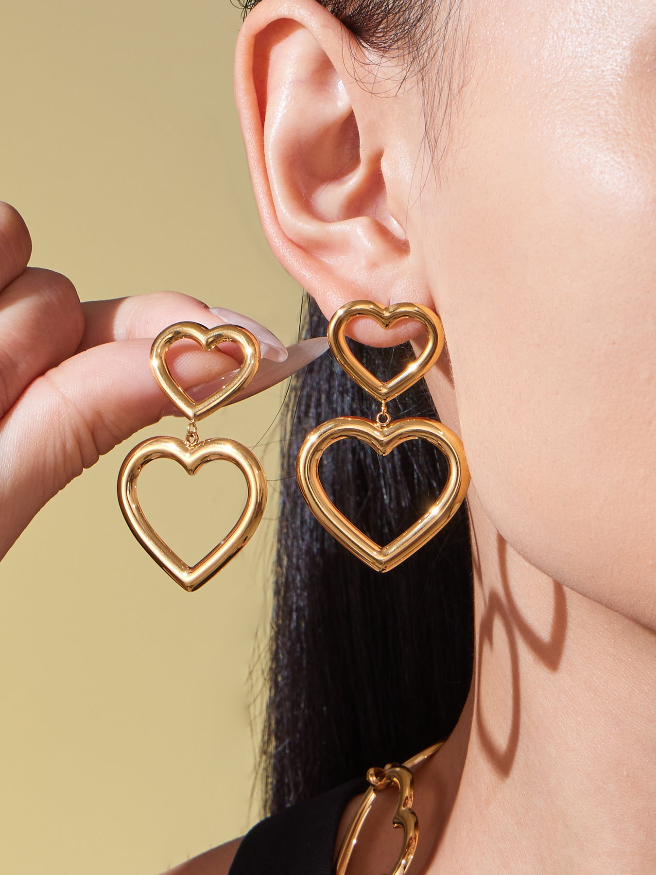 Model wearing gold heart hoop earrings with double open-heart design