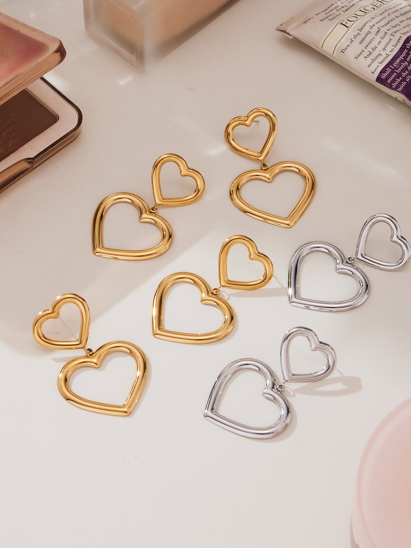 Open heart hoop earrings in gold and silver colors displayed flat, minimalist stainless steel jewelry