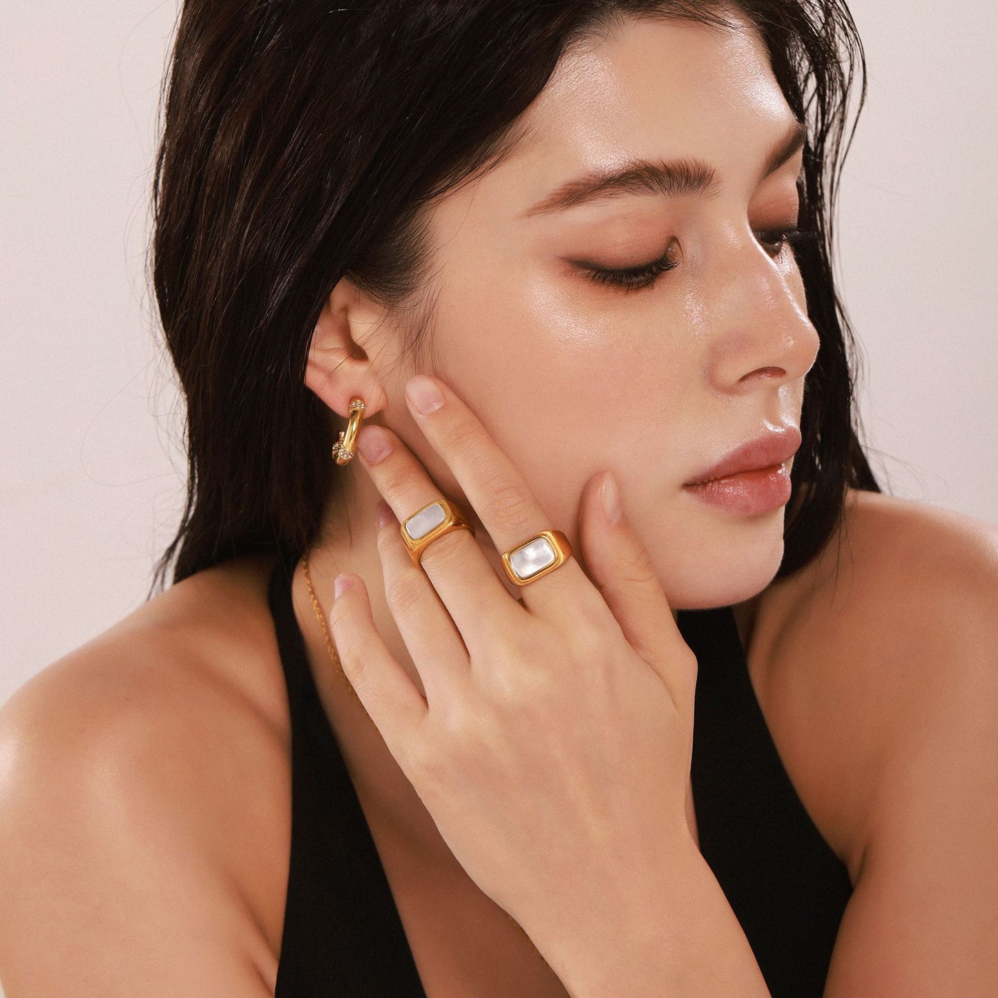 Woman wearing gold seashell pearl ring and matching earrings on a neutral background