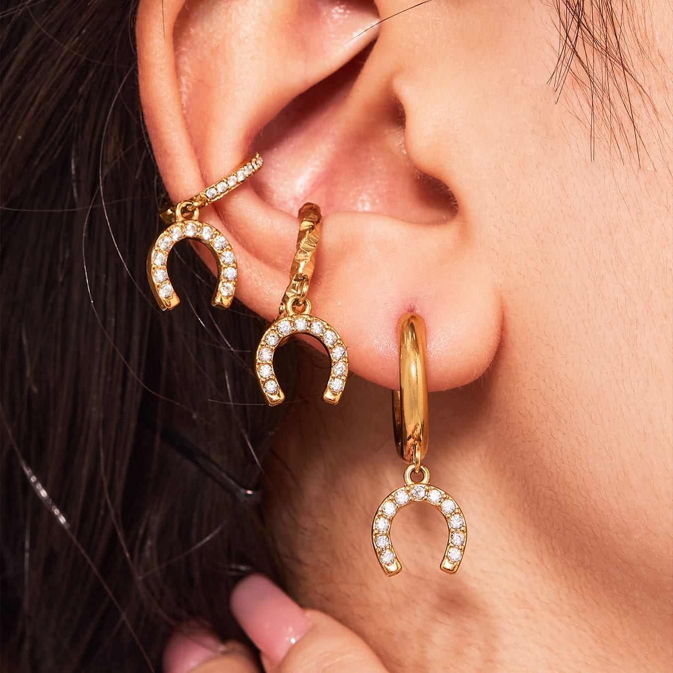 Gold hoop earrings with horseshoe charms worn by a person.