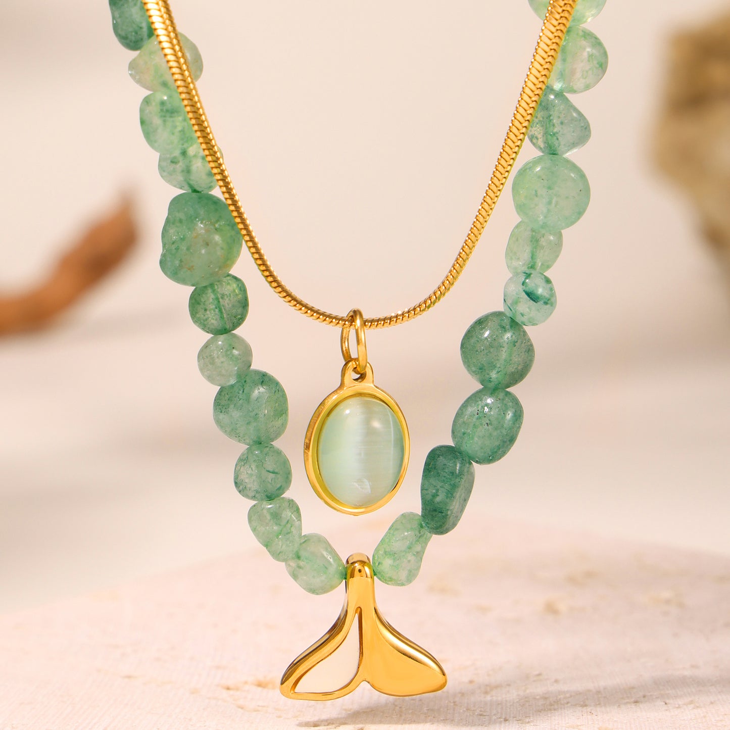 Green beaded necklace with gold pendant on a neutral background