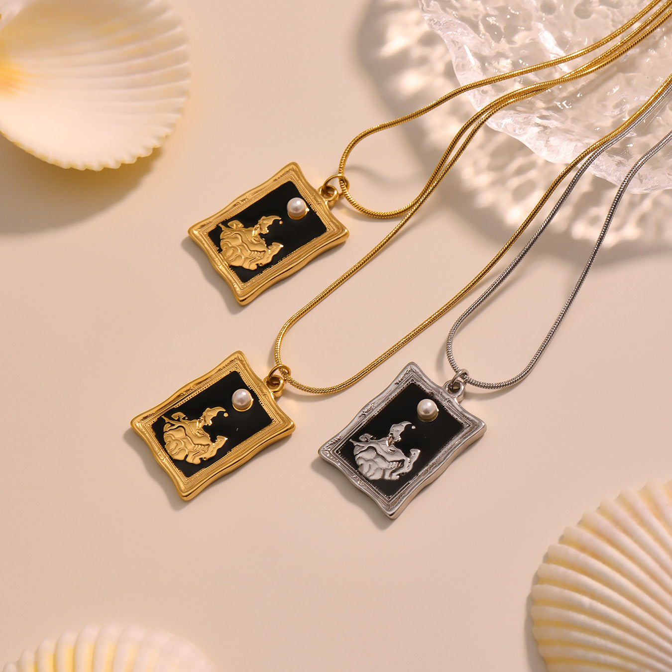 Two gold necklaces with black pendants featuring white figures on a beige surface with shell decorations.