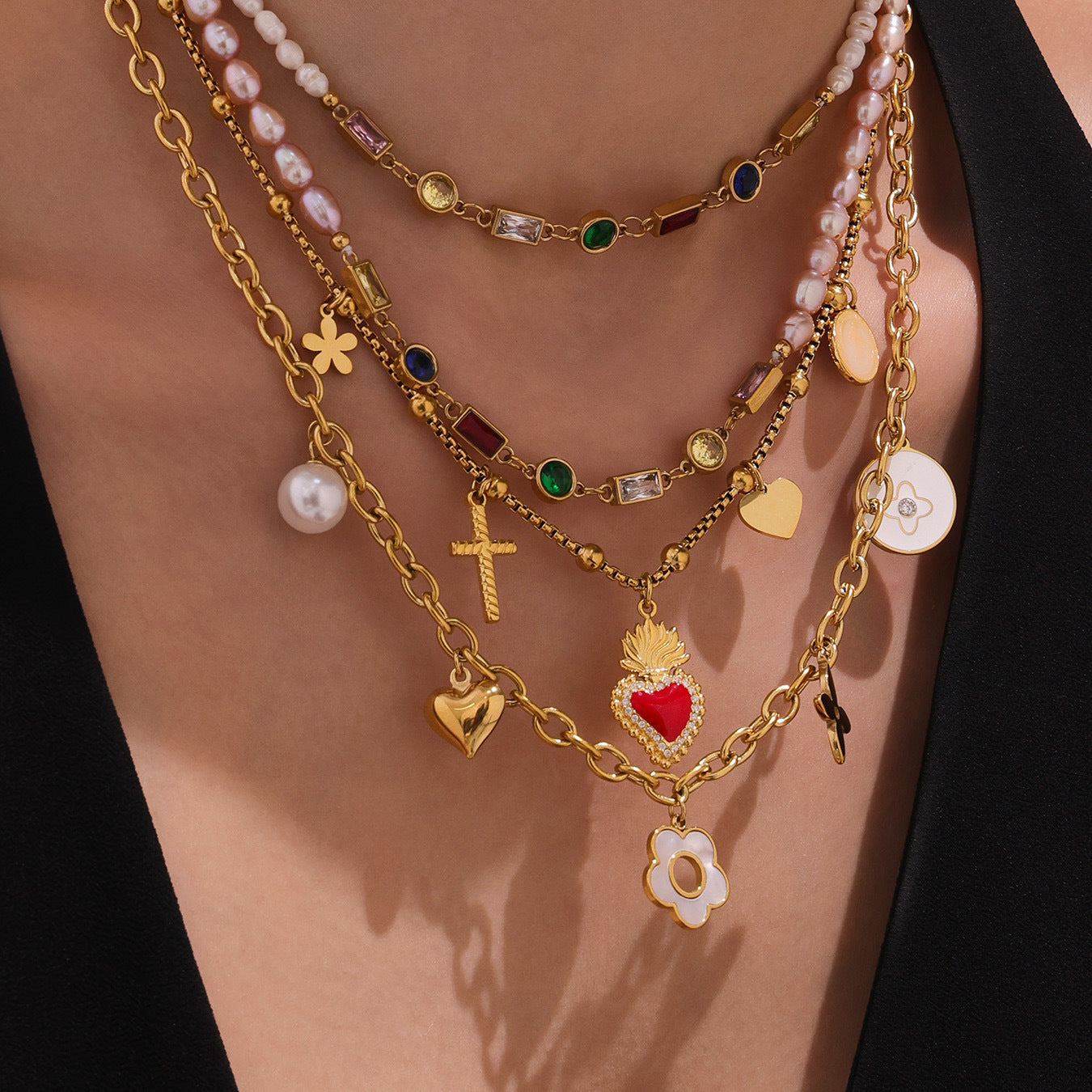 Layered gold necklaces with various charms on a person wearing a black top.