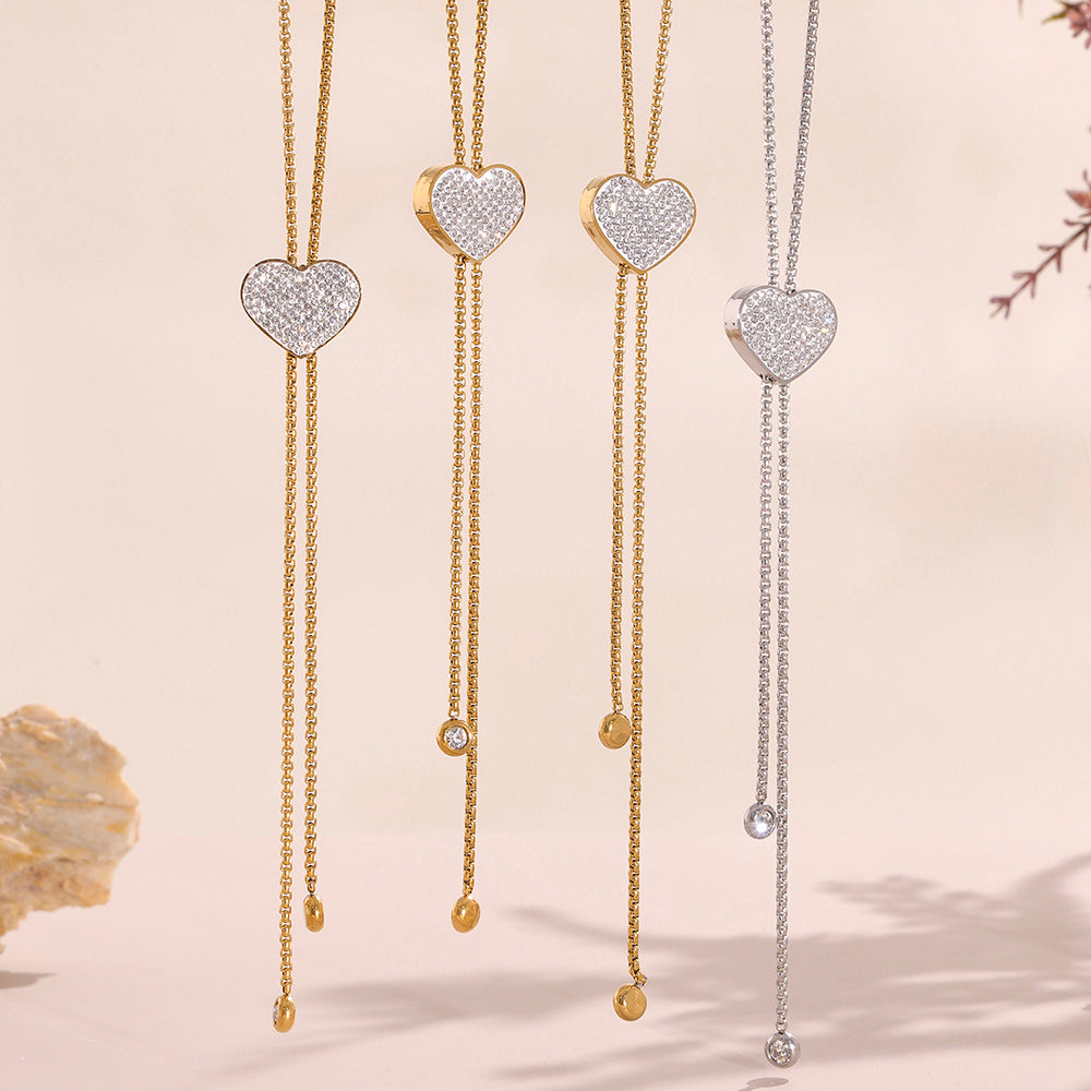 Heart-shaped diamond pendants on gold chains against a beige background