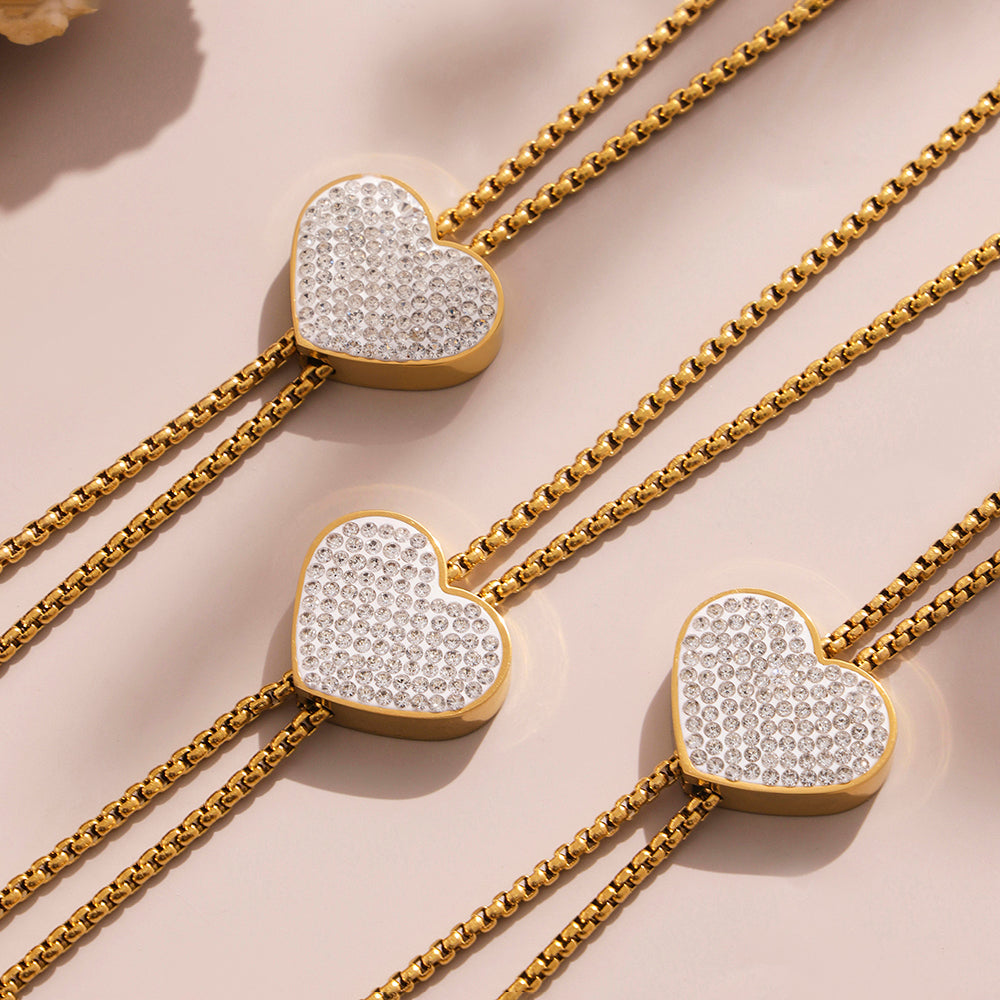 Three gold necklaces with heart-shaped diamond pendants on a beige background